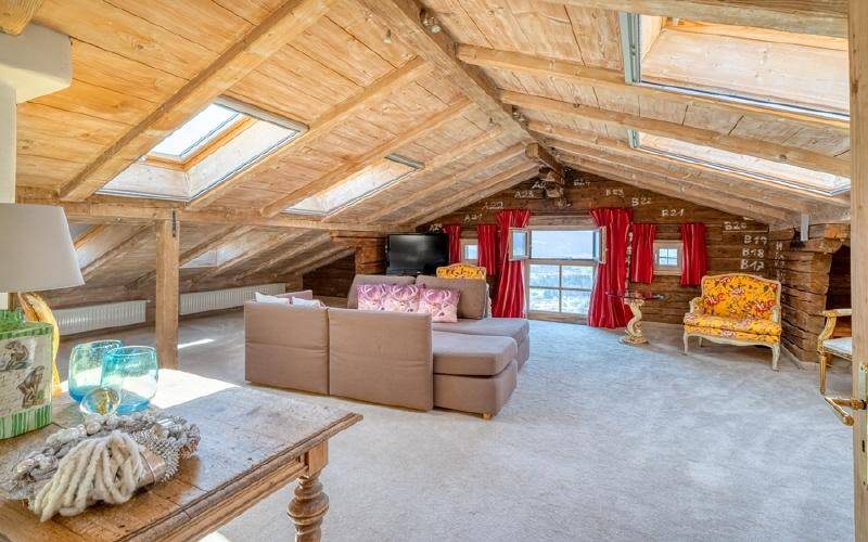 Heller Dachboden-Wohnbereich mit sichtbaren Holzbalken, Dachfenstern und Teppichboden.