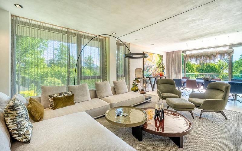 Helles Wohnzimmer mit großem Sofa, modernen Möbeln und raumhohen Fenstern mit Blick ins Grüne.