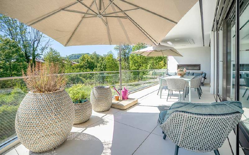 Geräumiger Balkon mit bequemen Sitzgelegenheiten, großem Sonnenschirm und weitem Blick ins Grüne.