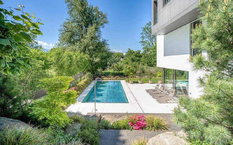 Außenpoolbereich mit Liegestühlen, umgeben von einer gepflegten Gartenanlage und moderner Architektur.