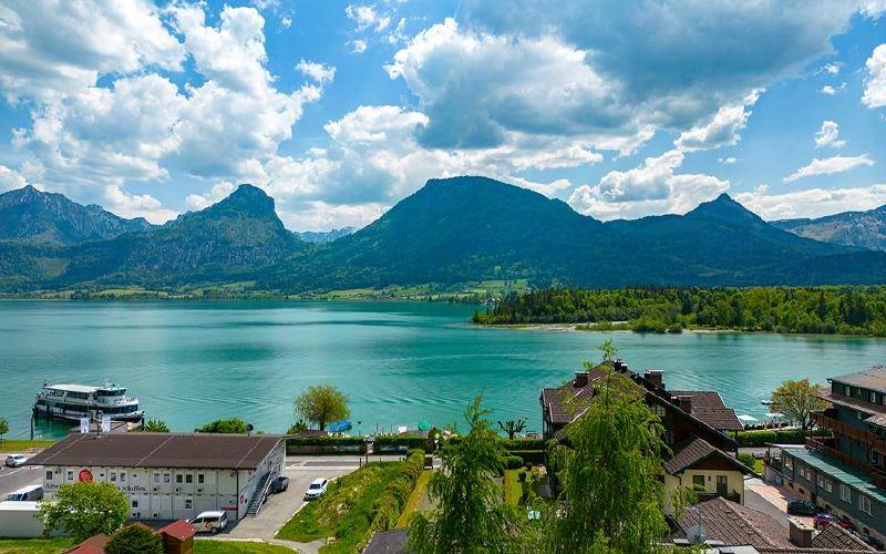 Atemberaubender Panoramablick auf einen malerischen See, umgeben von majestätischen Bergen unter blauem Himmel.