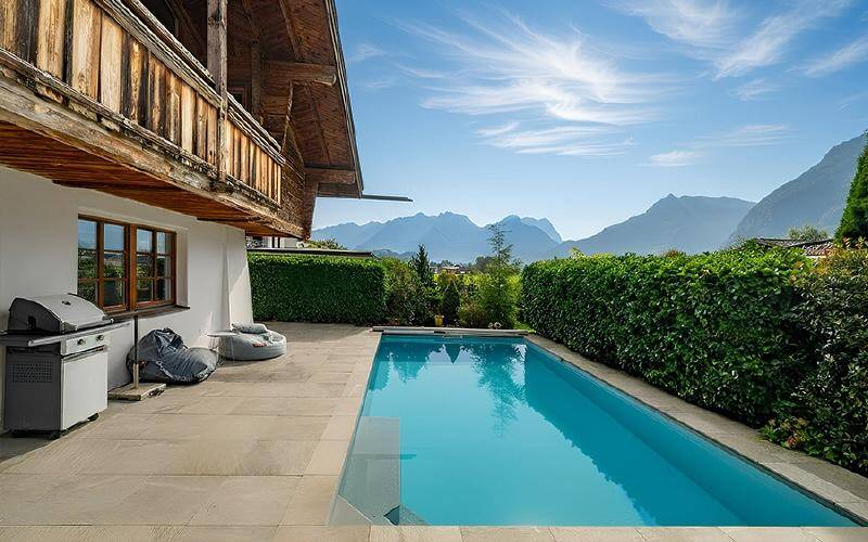 Großzügiger Außenpoolbereich mit Grillstation und Panoramablick auf die Berglandschaft.