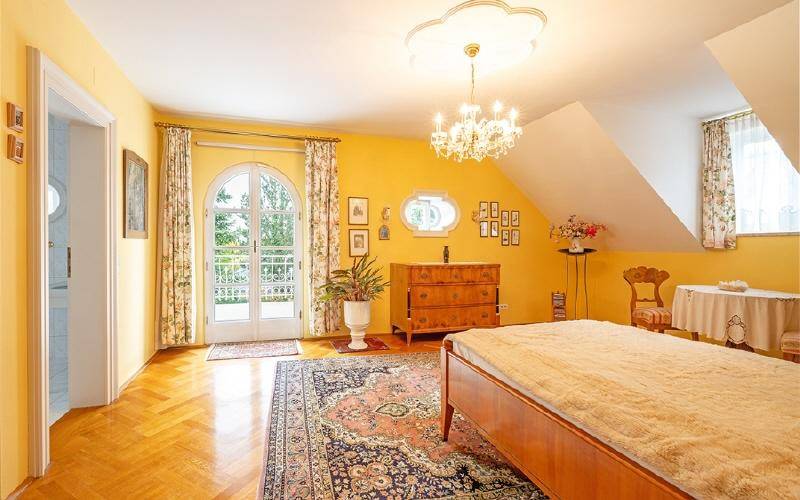 Helles Schlafzimmer mit Parkettboden, Kronleuchter und Balkonzugang.