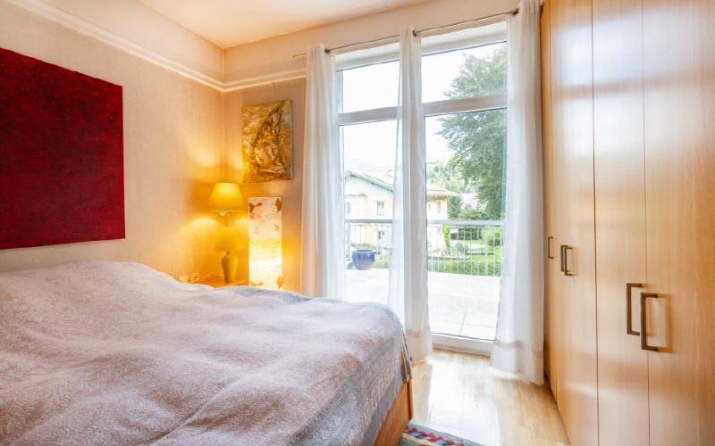 Helles Schlafzimmer mit Holzboden, Einbauschrank und Zugang zum Balkon.