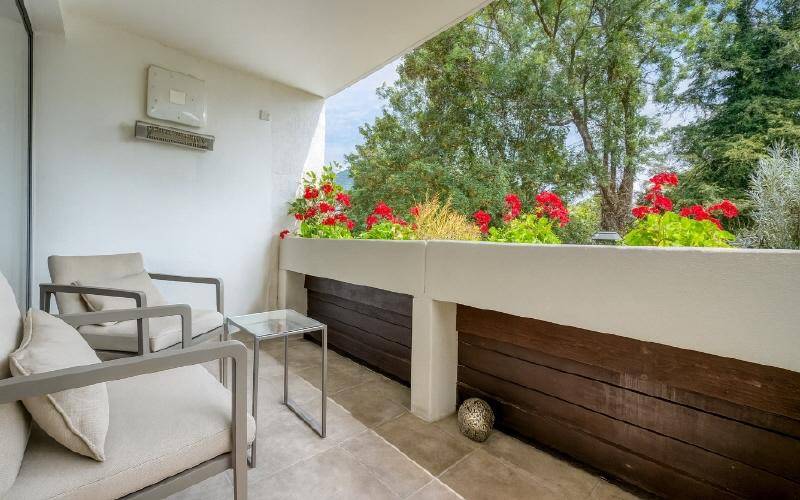 Heller Balkon mit bequemen Sitzgelegenheiten, Blumenkästen und Blick ins Grüne.