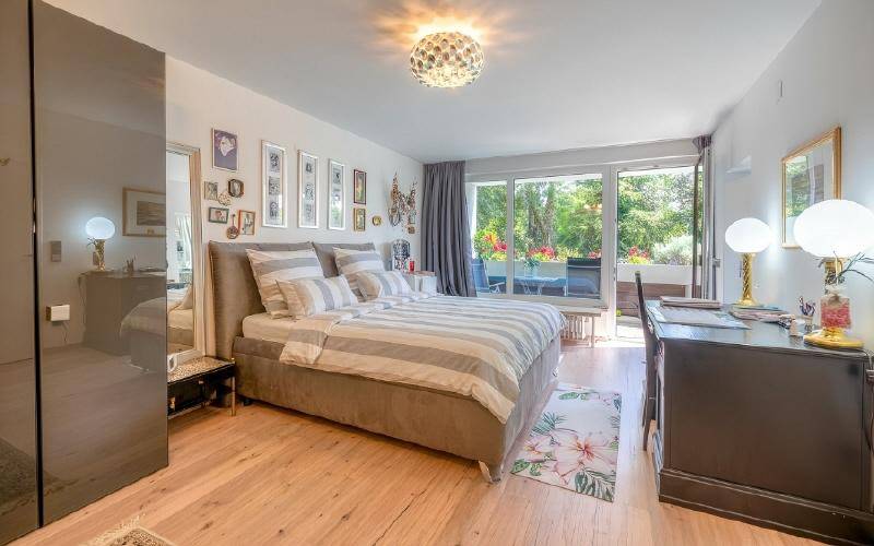 Helles Schlafzimmer mit Holzboden, großem Bett und Zugang zu einem Balkon.