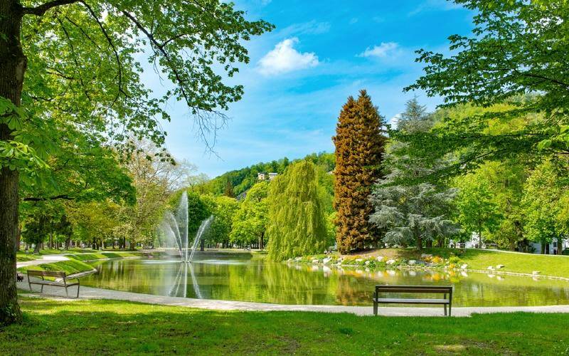 Malerischer Park mit Teich, Springbrunnen und üppiger grüner Vegetation.