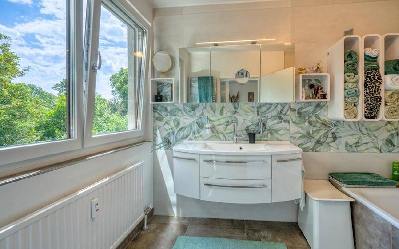 Modernes Badezimmer mit großem Fenster, Waschtisch und floraler Wandgestaltung.