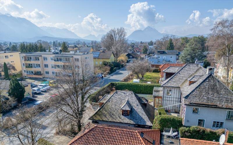 Luftaufnahme einer Wohngegend mit traditionellen Dächern und einer Bergkette im Hintergrund.