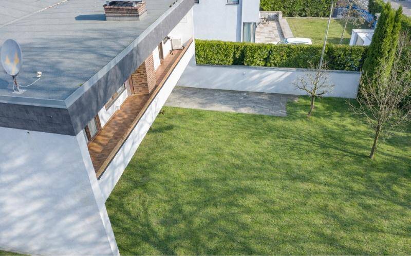 Gepflegter Rasenbereich neben einem modernen Gebäude mit Flachdach und einer kleinen Terrasse.