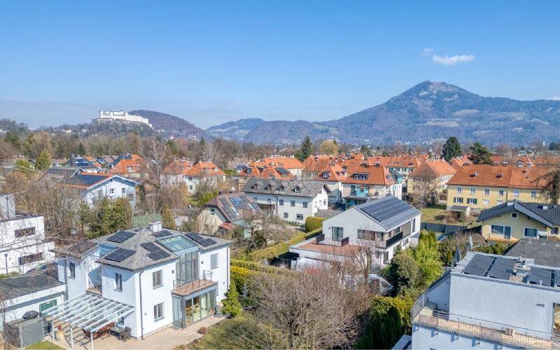 Panoramablick über eine Wohnsiedlung mit Bergen und einer historischen Festung im Hintergrund.