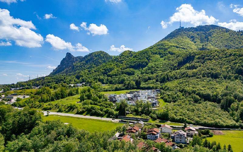 Luftaufnahme einer Wohnsiedlung eingebettet in eine grüne Berglandschaft mit weitem Blick.
