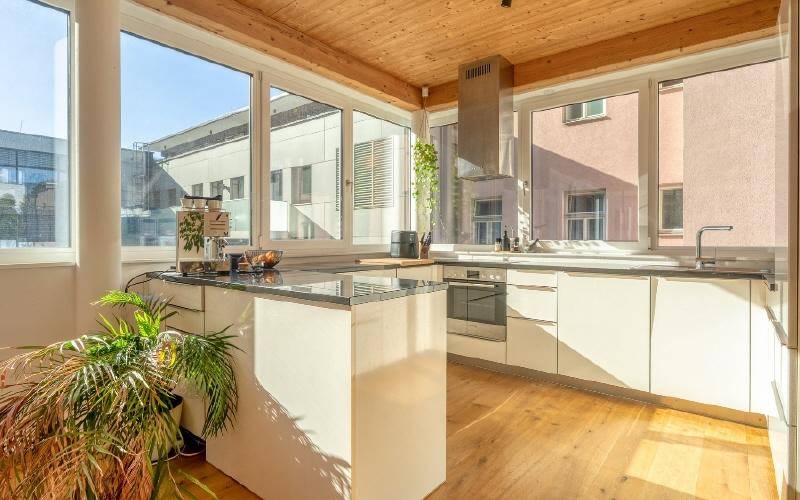 Moderne Küche mit weißen Schränken, dunkler Arbeitsplatte und großen Fenstern.