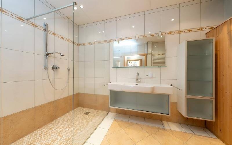 Helles Badezimmer mit großer begehbarer Dusche, modernem Waschtisch und Fliesenboden.