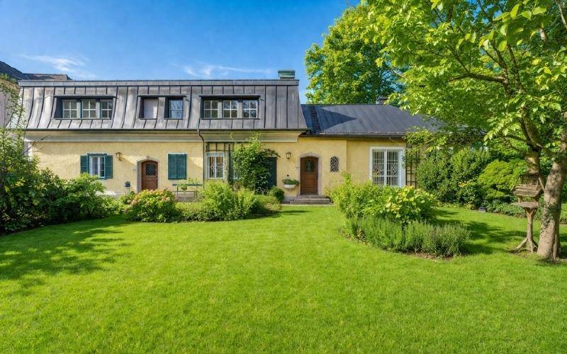 Gepflegter Garten mit Rasenfläche und altem Baumbestand vor dem historischen Wohnhaus.