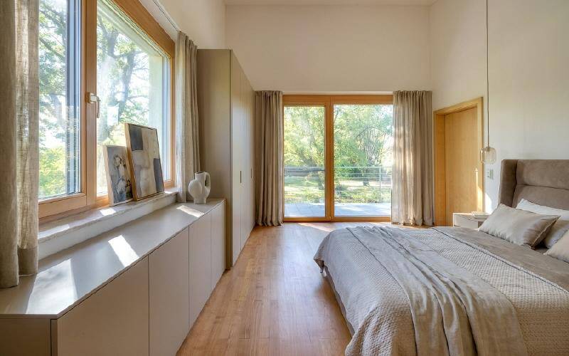 Helles Schlafzimmer mit Holzboden, großen Fenstern und Zugang zu einem Außenbereich mit Grünblick.