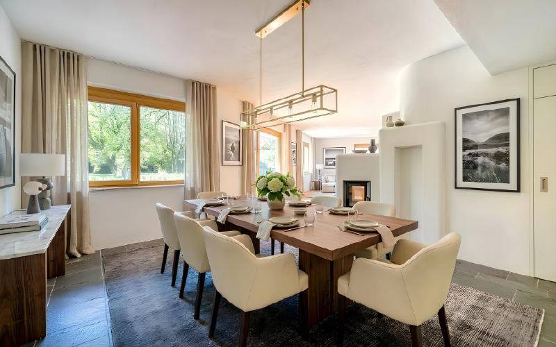 Eleganter Essbereich mit großem Holztisch, modernen Stühlen und Steinboden, hell beleuchtet mit Gartenblick.