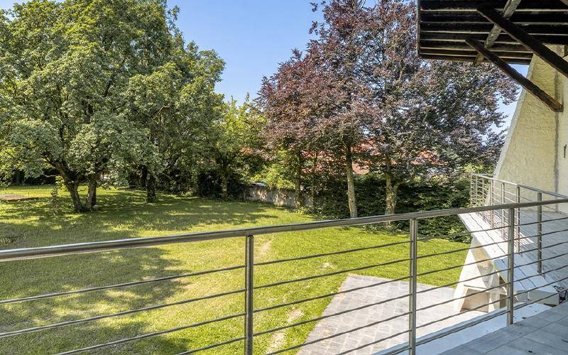 Balkon mit Edelstahlgeländer und weitem Blick auf den gepflegten, grünen Garten mit altem Baumbestand.