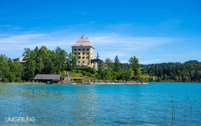 Historisches Gebäude am Ufer eines klaren Sees, umgeben von üppiger Natur und mit privatem Seezugang.