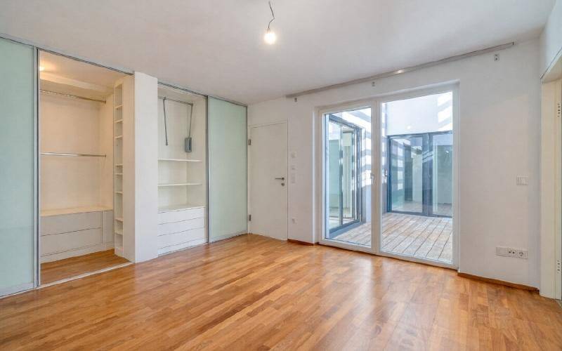 Helles Schlafzimmer mit Holzboden, Einbauschränken und Zugang zu einem Außenbereich.