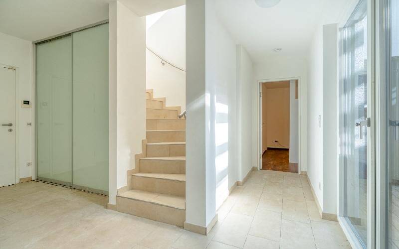 Heller Flur mit Fliesenboden, Treppe und Glasschiebetür.