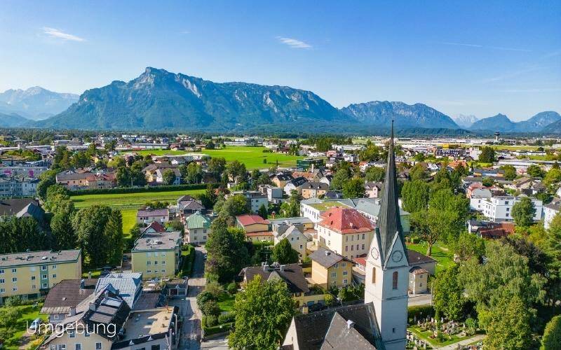 Panoramablick aus der Vogelperspektive auf eine malerische Stadt mit Kirche und majestätischer Bergkulisse.