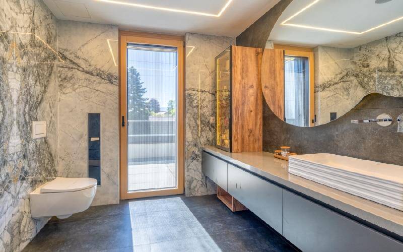 Luxuriöses Badezimmer mit Marmorwänden, modernem Waschtisch und wandhängendem WC.
