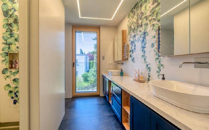 Modernes Badezimmer mit Doppelwaschbecken, floraler Tapete und Fenster zum Garten.