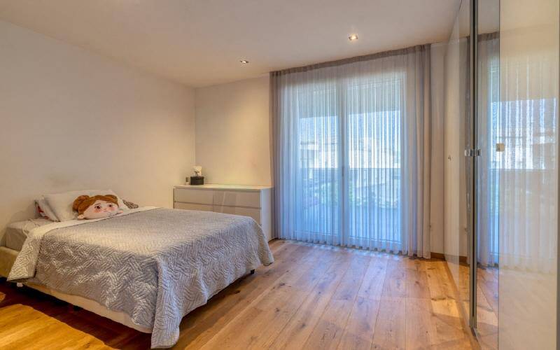 Kinderzimmer mit Holzboden, großen Fenstern und hellem Kleiderschrank.