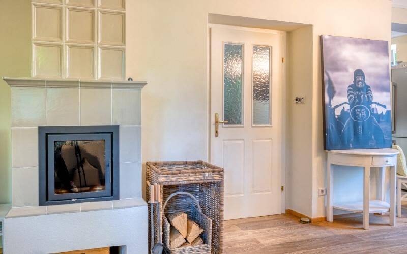 Detailansicht eines traditionellen Kachelofens mit Holzkorb und moderner Kunst an der Wand.