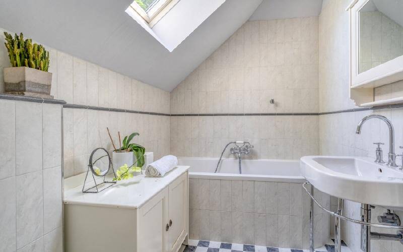 Badezimmer mit Badewanne, Dachfenster und kariertem Fliesenboden in Hell- und Dunkelgrau.