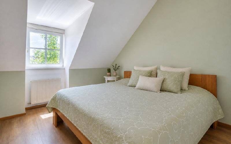 Helles Schlafzimmer mit Holzbett, Dachschräge und Fenster mit Blick ins Grüne.