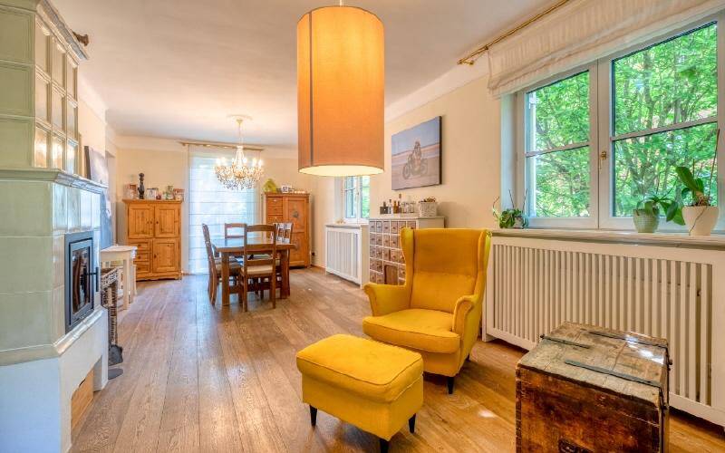 Helles Wohn- und Esszimmer mit Holzboden, Kachelofen und gemütlichem Sessel.