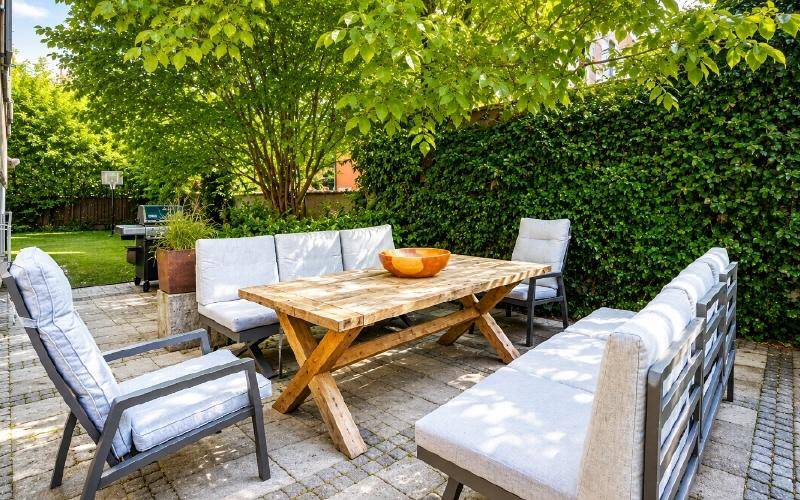 Gemütliche Terrasse mit Holztisch und bequemen Sitzgelegenheiten, umgeben von grünen Hecken.