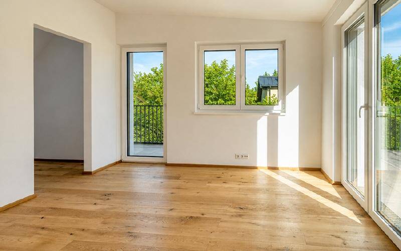 Heller, leerer Raum mit Eichenparkettboden, großen Fenstern und Zugang zum Balkon.