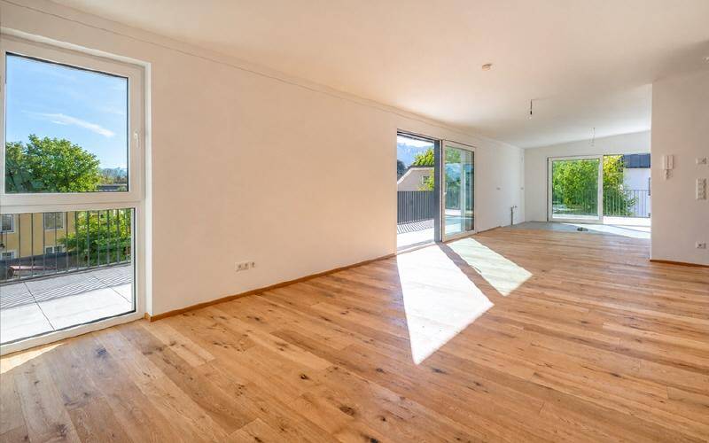 Lichtdurchfluteter, leerer Raum mit Holzboden und mehreren Zugängen zu Außenbereichen.