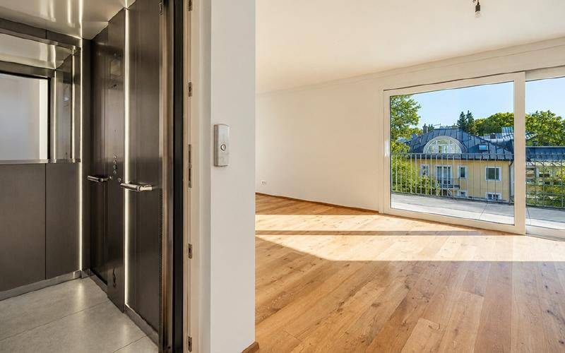 Moderner Aufzug und heller Innenraum mit Holzboden und großen Schiebetüren.