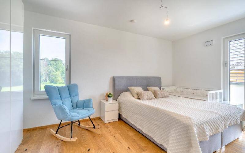 Helles Schlafzimmer mit Holzboden, großem Fenster und Blick ins Grüne.