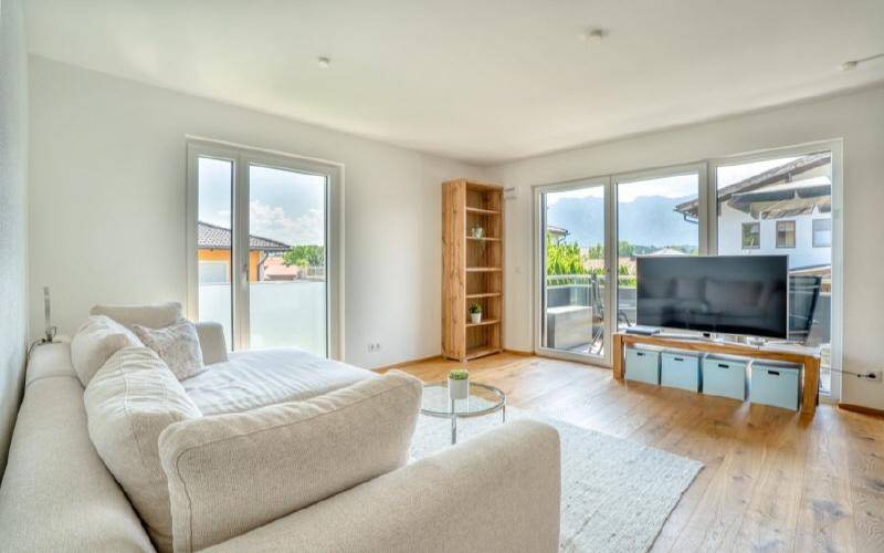 Helles Wohnzimmer mit Holzboden, großzügigen Fenstern und Zugang zu einem Außenbereich.