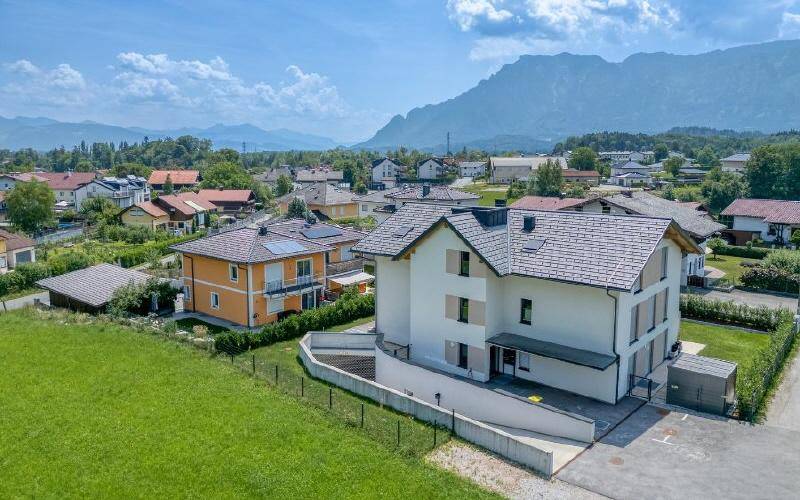Luftaufnahme eines modernen Wohnhauses mit umliegenden Grünflächen und Bergblick.