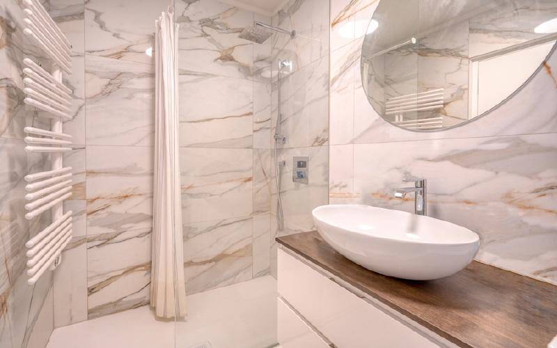 Modernes Badezimmer mit eleganten Marmorfliesen, ebenerdiger Dusche und stilvollem Aufsatzwaschbecken.