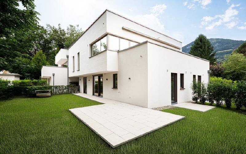 Moderne weiße Villa mit Flachdach, großen Fenstern und gepflegtem Gartenbereich.