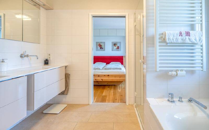 Modernes Badezimmer mit Doppelwaschbecken, Badewanne und Blick ins angrenzende Schlafzimmer.