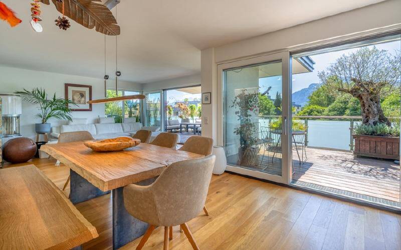 Heller Essbereich mit großem Holztisch, verbunden mit Wohnzimmer und Terrasse mit Bergblick.