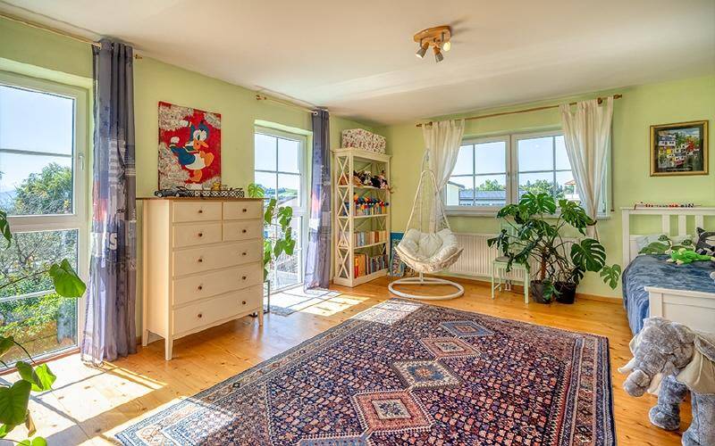 Helles Schlafzimmer mit Holzboden, großen Fenstern und einem gemütlichen Hängesessel.