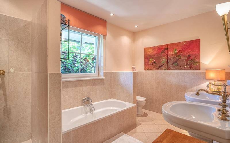Badezimmer mit Badewanne, Doppelwaschbecken und Fenster, in hellen Beigetönen gehalten.