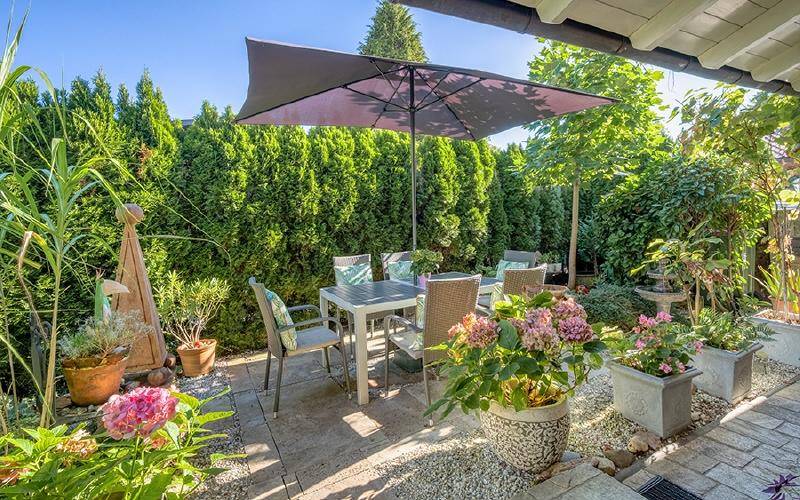 Gemütliche Terrasse mit Esstisch, Sonnenschirm und üppiger Bepflanzung.