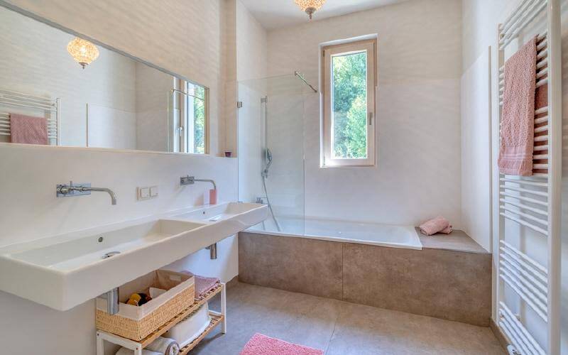 Modernes Badezimmer mit Doppelwaschbecken, Badewanne, Dusche und Fenster für Tageslicht.