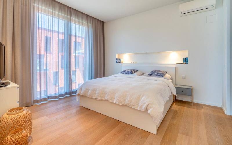 Helles Schlafzimmer mit Holzboden, großem Fenster, integrierter Beleuchtung und Klimaanlage.