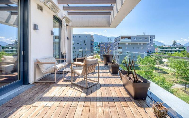 Geräumiger Balkon mit Holzdeck, Glasgeländer und Panoramablick auf die Berge und Umgebung.